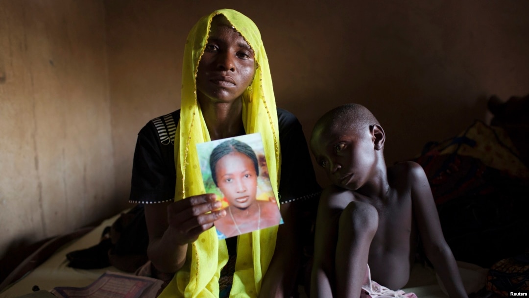 Rachel Daniel, 35, holds up a picture of her abducted daughter Rose Daniel, 17, as her son Bukar, 7, sits beside her at her home in Maiduguri, Nigeria, May 21, 2014. 