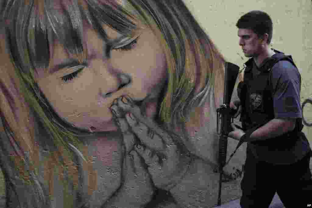 A police officer walks past a graffiti during a police operation in the Nova Holanda slum, part of the Complexo da Mare, in Rio de Janeiro, Brazil. 