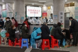 FILE - People wait as medical staff, seen in back, wear protective clothing to help stop the spread of a deadly virus which began in the city, at Wuhan Red Cross Hospital in Wuhan, Jan. 24, 2020.