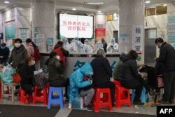 FILE - People wait as medical staff, seen in back, wear protective clothing to help stop the spread of a deadly virus which began in the city, at Wuhan Red Cross Hospital in Wuhan, Jan. 24, 2020.