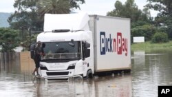 FILE - A person stands on the bumper of a delivery vehicle in flood waters in Ladysmith, KwaZulu Natal Province Monday, Jan 17, 2022.