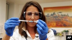 Dr Felicity Hartnell, who is a clinical research fellow at Oxford University, holds a vial of an experimental vaccine against Ebola in Oxford, England Wednesday Sept. 17, 2014. A former nurse will be the first of 60 healthy volunteers in the UK who will receive the vaccine. The vaccine was developed by the U.S. National Institutes of Health and GlaxoSmithKline and targets the Zaire strain of Ebola, the cause of the ongoing outbreak in West Africa. A trial of the same vaccine has already begun in the U.S. (AP Photo/Steve Parsons/Pool)