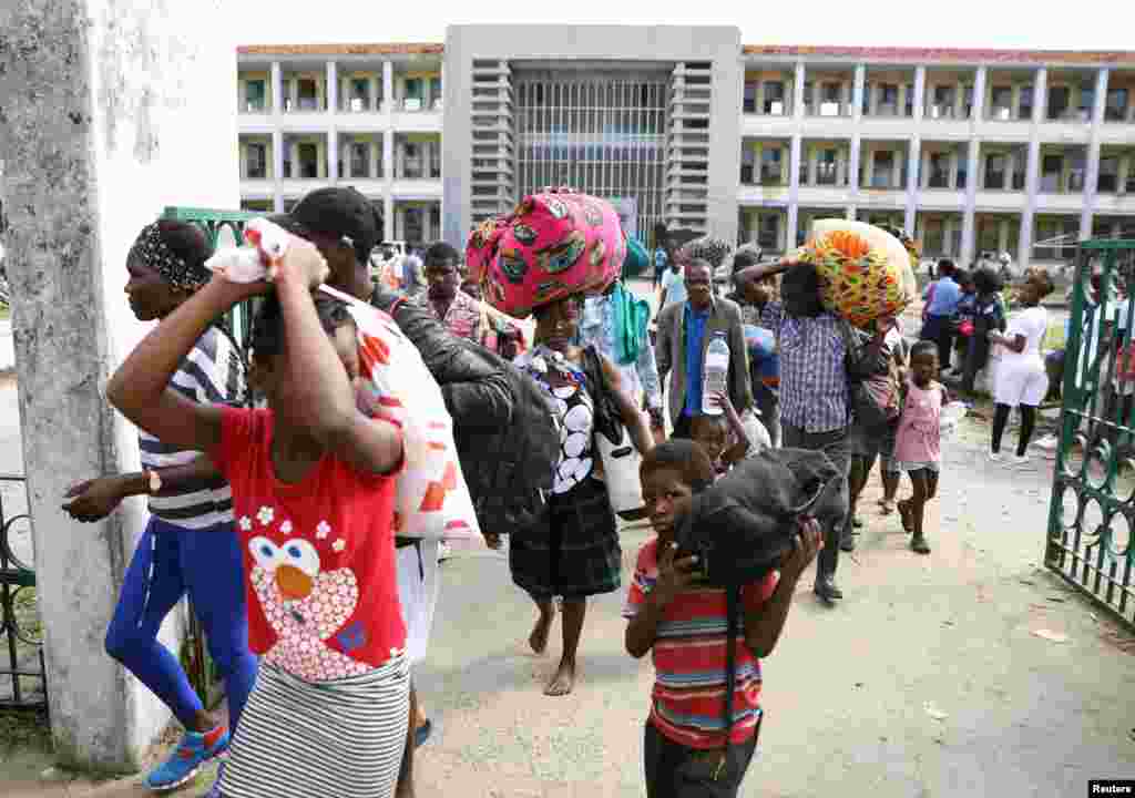 Pessoas evacuadas de Buzi carregam os seus bens À saída de uma escola que foi usada como centro para deslocados depois do ciclone Idai, ter atingido a Beira, Moçambique, 25 de Março, 2019.