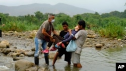 Una mujer venezolana es ayudada por tres hombres a cruzar ilegalmente a Colombia desde Venezuela, cerca del Puente Internacional Simón Bolívar en La Parada, cerca de Cúcuta, Colombia, el sábado 14 de marzo de 2020.