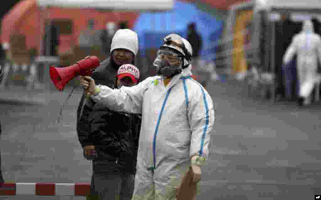 An official wearing a protective suit helps usher people through a radiation emergency scanning center in Koriyama, Japan, Tuesday, four days after a giant quake and tsunami struck the country's northeastern coast, March 15, 2011 – (AP)
