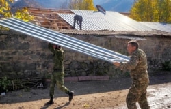 Garo Dadevusyan, right, wrenches off its metal roof and prepares to set the stone house on fire in Kalbajar before leaving the separatist region of Nagorno-Karabakh for Armenia, Nov. 14, 2020. The village is to be turned over to Azerbaijan Nov. 15.