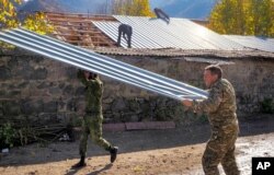 Garo Dadevusyan, right, wrenches off its metal roof and prepares to set the stone house on fire in Kalbajar before leaving the separatist region of Nagorno-Karabakh for Armenia, Nov. 14, 2020. The village is to be turned over to Azerbaijan Nov. 15.