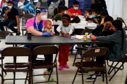 FILE - Migrants pass the time at a migrant shelter, May 12, 2021, in McAllen, Texas.