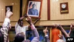 People remove, from the wall at the International Conference centre, where parliament had their sitting, the portrait of former Zimbabwean President Robert Mugabe after his resignation on November 21, 2017, in Harare. Robert Mugabe resigned as president of Zimbabwe on November 21, 2017 swept from power as his 37-year reign of brutality and autocratic control crumbled within days of a military takeover. The bombshell news was delivered by the parliament speaker to a special joint session of the assembly which had convened to impeach Mugabe, 93, who has dominated every aspect of Zimbabwean public life since independence in 1980. AFP PHOTO /Jekesai NJIKIZANA