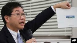 Japan Sport Council Administration officer Takakuni Ikeda shows a proposal brochure by one of two groups competing to build the new Tokyo Olympic stadium during a news conference in Tokyo, Dec. 14, 2015.