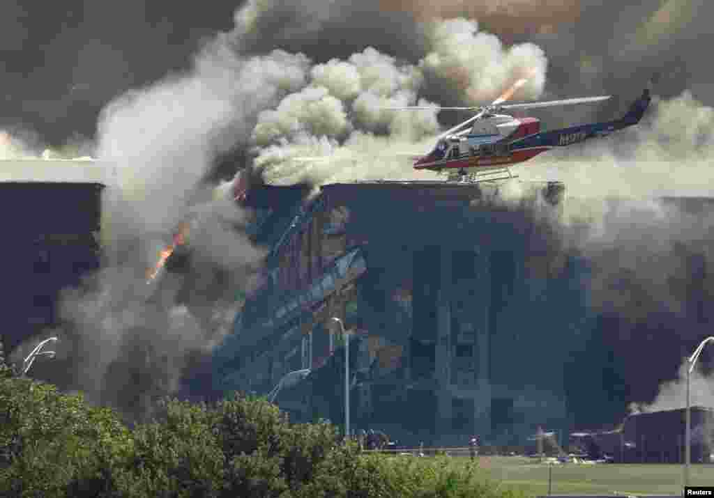 A rescue helicopter surveys damage to the Pentagon as firefighters battle flames after an airplane crashed into the U.S. military Headquarters outside Washington, D.C.
