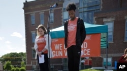 FILE - Kait Saier, left, and Kamren Baxter, right, observe a moment of silence while standing near shoes arranged in the shape of a peace sign to honor shooting homicide victims during a rally against gun violence, June 3, 2018, in Boston.