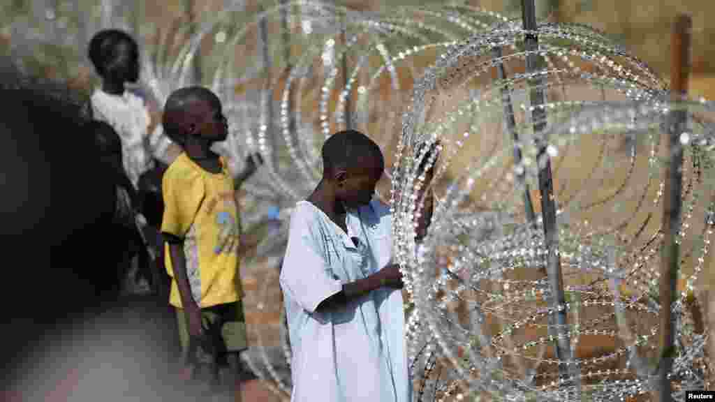 Meninos deslocados ao lado do arame farpado dentro do cmapo de refugiados instalado pela Missão das Nações Unidas no Sudão (UNMIS) em Juba Dez 19, 2013. O governo do Sudão do Sul tem combatido para reconquistar o control da cidade. 