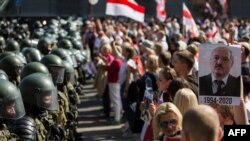 Belarusian security forces block a street during an opposition rally challenging official presidential elections results, in Minsk, Belarus, Aug. 30, 2020. The poster depicts President Alexander Lukashenko and the years he has been in power.