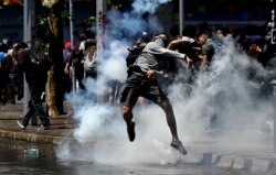 FILE - A protester returns a tear gas canister to police during clashes in Santiago, Chile, Oct. 21, 2019.