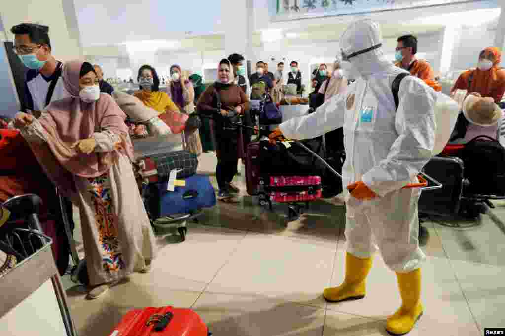 A traveler reacts as a worker puts disinfectant on passengers&#39; bags at the international arrivals terminal of Soekarno-Hatta Airport near Jakarta, Indonesia, during the coronavirus outbreak.