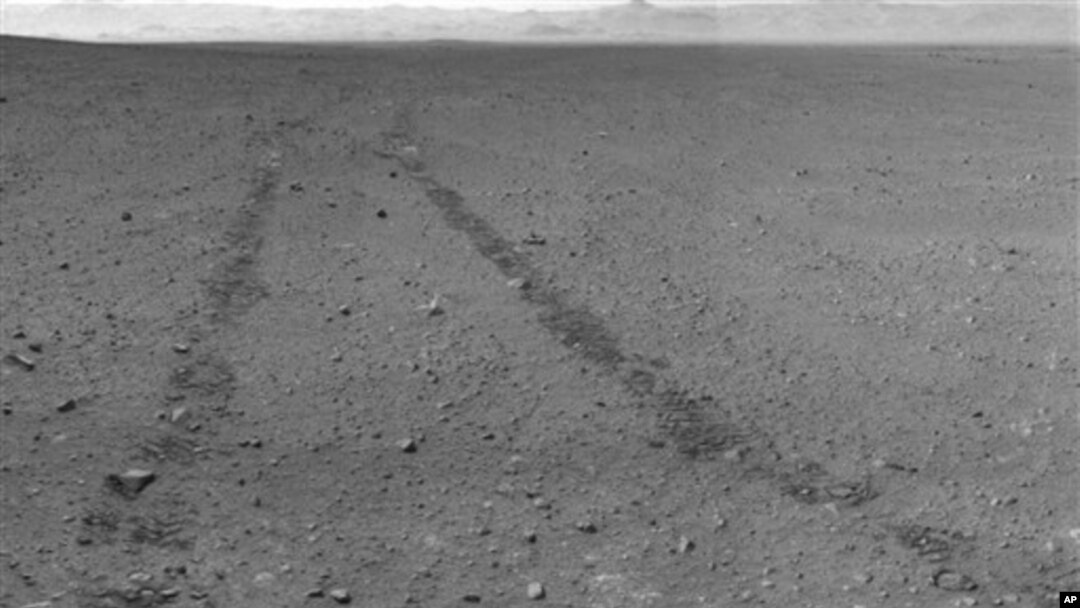 Crno-bela fotografija tragova točkova marsovskog rovera Kjuriositi u pesku crvene planete