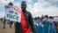 FILE - South Sudanese people hold signs as they await the arrival back in the country of South Sudan's President Salva Kiir, at the airport in Juba, South Sudan, June 22, 2018. 