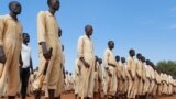 FILE - Men stand at attention with the wooden mock guns they use to train with, at a military training center in Owiny Ki-Bul, Eastern Equatoria, South Sudan, June 27, 2020.