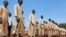 FILE - Men stand at attention with the wooden mock guns they use to train with, at a military training center in Owiny Ki-Bul, Eastern Equatoria, South Sudan, June 27, 2020.