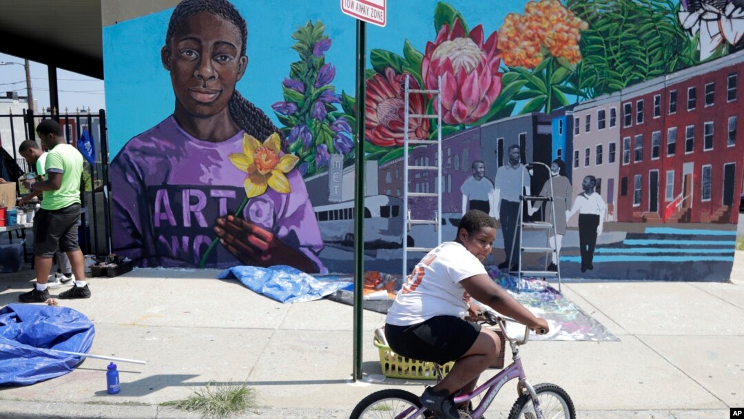 Seorang anak bersepeda melintas di depan mural di Gereja New Song Community di distrik Sandtown, Baltimore, 29 Juli 2019. (Foto: AP)
