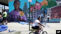 Seorang anak bersepeda melintas di depan mural di Gereja New Song Community di distrik Sandtown, Baltimore, 29 Juli 2019. (Foto: AP)