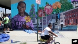 Un niño monta su bicicleta el lunes 29 de julio de 2019 después de ofrecerse como voluntario para pintar un mural afuera de la Iglesia de la Comunidad New Song en la sección Sandtown de Baltimore. (Foto AP / Julio Cortez)