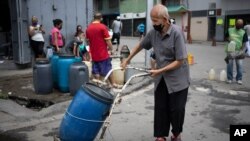 Un hombre, con tapabocas, empuja un recipiente lleno de agua que recogió de un grifo de la calle en una carretilla, en Caracas, Venezuela. Junio 20, 2020.