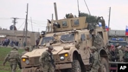 In this frame grab from video, people and soldiers gathering next to an American military convoy stuck in the village of Khirbet Ammu, east of Qamishli city, Syria, Feb. 12, 2020. 