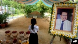 In this Nov. 20, 2016 photo, a girl stands by a portrait of Kem Ley, a Cambodian prominent political analyst, at his grave in Ang Takok, Cambodia. Kem Ley, a poor rice farmer's son turned champion of Cambodia's have-nots, was sipping his usual iced latte in the same chair he had occupied most mornings for years when a former soldier he may never have met walked into the Caltex gas station cafe. Armed with a semi-automatic Glock pistol, the assassin fired into his chest and head, execution-style. Then he walked casually away from the scene. (AP Photo/Denis Gray)