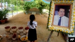 In this Nov. 20, 2016 photo, a girl stands by a portrait of Kem Ley, a Cambodian prominent political analyst, at his grave in Ang Takok, Cambodia. Kem Ley, a poor rice farmer's son turned champion of Cambodia's have-nots, was sipping his usual iced latte in the same chair he had occupied most mornings for years when a former solider he may never have met walked into the Caltex gas station cafe. Armed with a semi-automatic Glock pistol, the assassin fired into his chest and head, execution-style. Then he walked casually away from the scene. (AP Photo/Denis Gray)