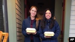 In this April 13, 2020 photo provided by Jay Peak Resort, Paula Davis, left, from Argentina, and Antonella Atto, from Peru, pose at the resort in Jay, Vt., with meals provided by The Belfry.