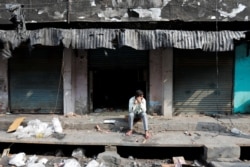 A man sits in front of burnt out properties owned by Muslims in a riot affected area following clashes between people demonstrating for and against a new citizenship law in New Delhi, India, March 2, 2020.