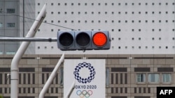 A red traffic light lights up on a street near the Tokyo Metropolitan Government Building displaying a banners of Tokyo 2020 Olympics Games in Tokyo on May 31, 2021.