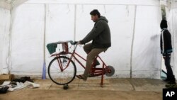 Syrian refugee Odai Ahmed peddles to charge smart phones and batteries inside a tent at the migrants camp near Calais, northern France, Nov. 4, 2015.