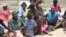 Women and their children in Mutare West wait as food is being cooked in December 2015 under FAO’s Livelihoods and Food Security Program in Zimbabwe.