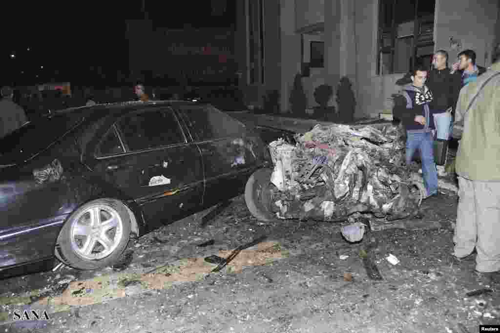 People stand near a damaged car and debris after explosions went off at the main gate of the Syrian Interior Ministry in Damascus December 12, 2012. 