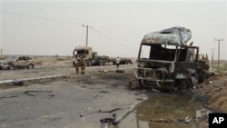 Soldiers stand by a burned out military vehicle at the site of an attack in Aden, Yemen, July 24, 2011. A suicide attacker driving a pickup truck packed with explosives blew himself up outside an army camp in Yemen's coastal city of Aden, killing at least