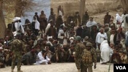 Pasukan nasional Afghanistan mengawasi ratusan warga Afghanistan yang berkumpul di luar pangkalan militer AS di distrik Panjwai, Kandahar pasca insiden penembakan (11/3).