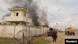 FILE - A member of the Afghan security forces walks as smoke billows from a building after a Taliban attack in Gereshk district of Helmand province, Afghanistan, March 9, 2016.