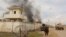FILE - A member of the Afghan security forces walks as smoke billows from a building after a Taliban attack in Gereshk district of Helmand province, Afghanistan, March 9, 2016.