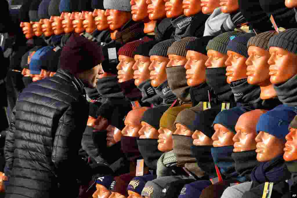 A man looks at himself in a mirror, hidden between mannequins, as he chooses a cap at the clothing market in Minsk, Belarus.