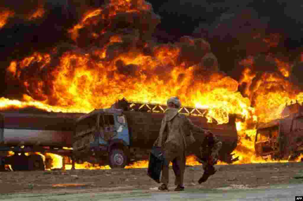 An Afghan carries his belongings as he passes burning fuel tankers in the outskirts of Kabul, Afghanistan, Thursday, Aug. 4, 2011. Police said around five fuel tankers carrying fuel for NATO and U.S. forces in Afghanistan caught fire inside a depot in Kab