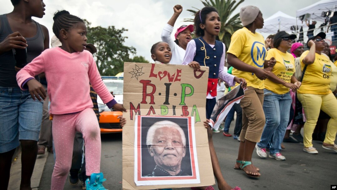 Anak-anak memegang poster Mandela bertuliskan Madiba, nama dimana ia biasa dipanggil di Afrika Selatan, berpawai bersama warga di dekat rumah Mandela di Soweto, Johannesburg 6/12/2013.