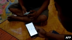 FILE - Young men use their mobile phones in Naypyidaw on March 16, 2021, as Myanmar military authorities ordered telecommunication companies to restrict services on their mobile data networks.