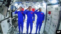 In this photo released by China's Xinhua News Agency, Chinese astronauts, from left; Tang Hongbo, Nie Haisheng, and Liu Boming salute from aboard China's space station core module Tianhe during a video conversation with Chinese President Xi Jinping,…