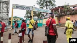 FILE - People, some wearing masks, walk by the entrance to Yaounde General Hospital, in Yaounde, Cameroon, March 6, 2020, amid the coronavirus pandemic. 