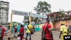 FILE - People, some wearing masks, walk by the entrance to Yaounde General Hospital, in Yaounde, Cameroon, March 6, 2020, amid the coronavirus pandemic. 