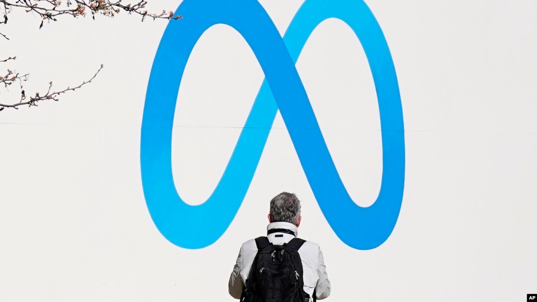 FILE - A person stands in front of a Meta sign outside of the company's headquarters in Menlo Park, Calif., March 7, 2023. 