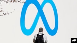 FILE - A person stands in front of a Meta sign outside of the company's headquarters in Menlo Park, Calif., March 7, 2023. 